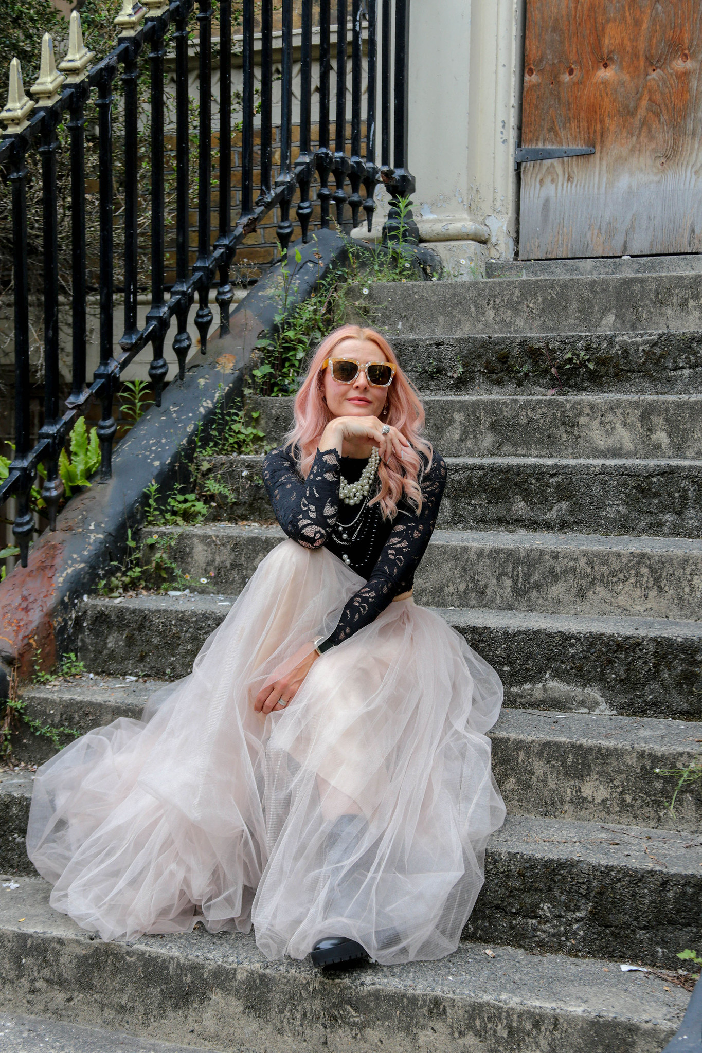 Giles Caldicott Photography: Catherine Summers AKA Not Dressed As Lamb | Wearing: cropped, long sleeve black lace top, pearl-effect square sunglasses, nude tulle maxi skirt, black lace-up boots | Sitting on the steps leading up to a boarded-up abandoned London town house
