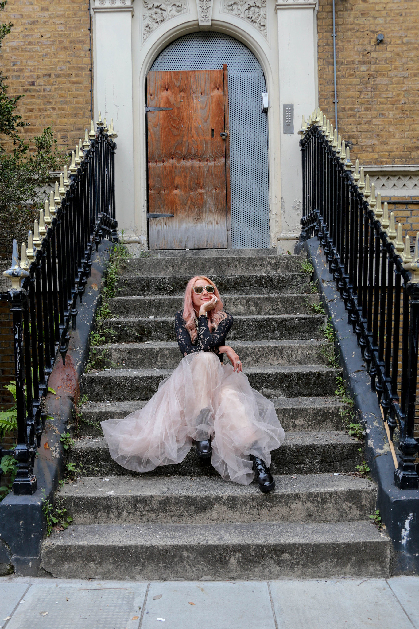 Giles Caldicott Photography: Catherine Summers AKA Not Dressed As Lamb | Wearing: cropped, long sleeve black lace top, pearl-effect square sunglasses, nude tulle maxi skirt, black lace-up boots | Sitting on the steps leading up to a boarded-up abandoned London town house