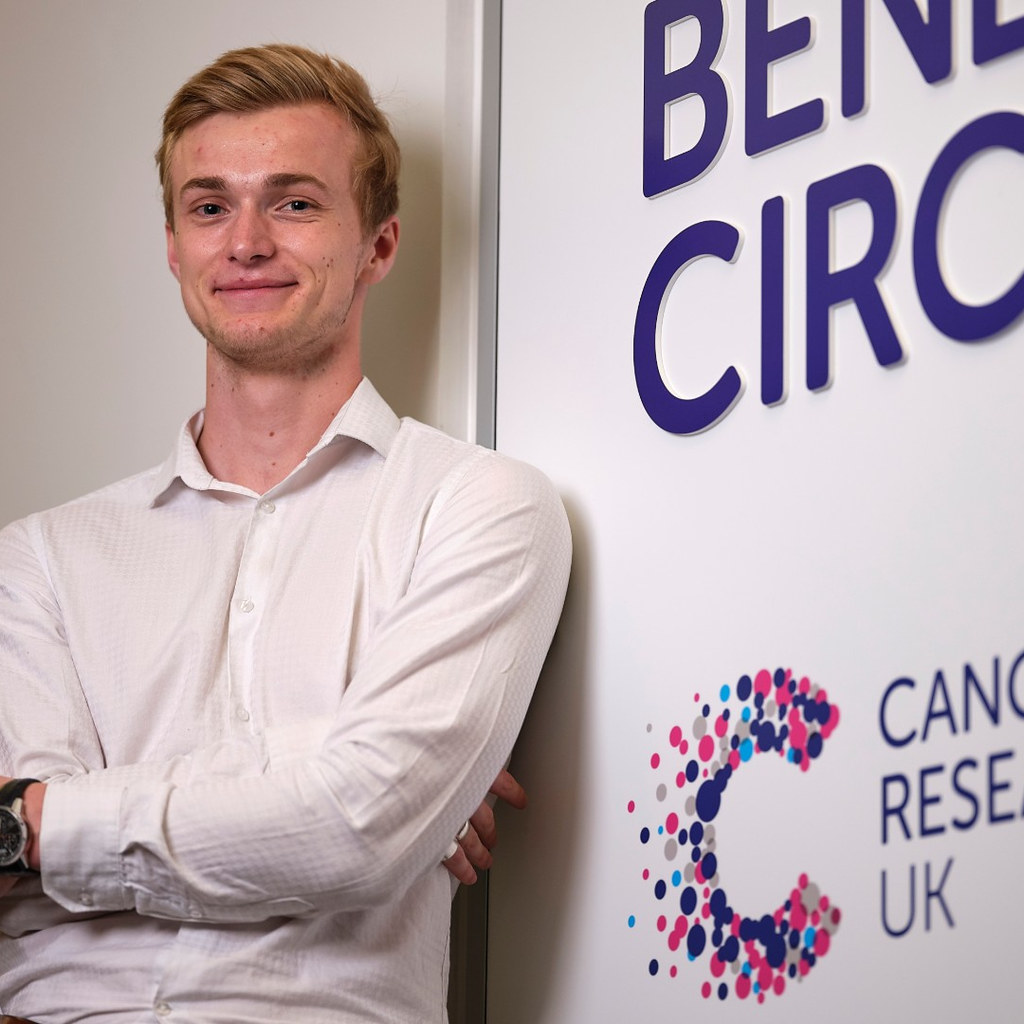 A young man stood in front of a Cancer Research UK sign.