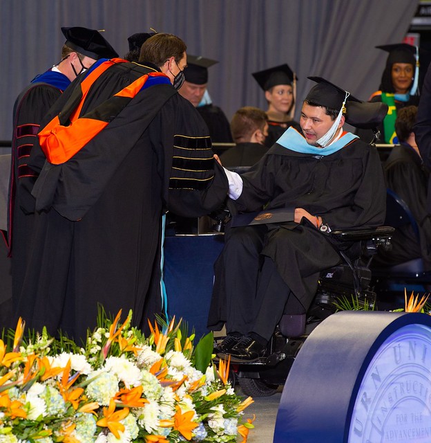 Matt Beth shakes hands with Auburn Board of Trustees member Clark Sahlie on stage at summer commencement.