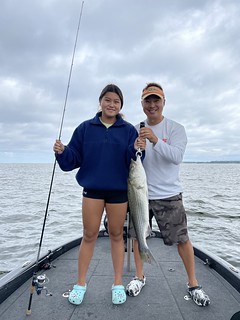 Photo of man and young woman on a boat holding a striped bass