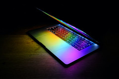 Open laptop isolated on dark wooden table with rainbow colors reflecting on keyboard