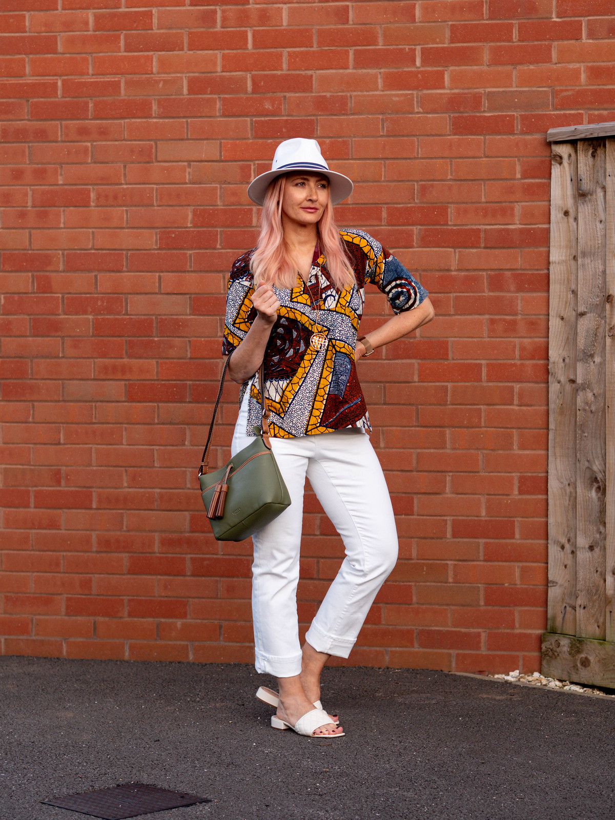 Catherine Summers AKA Not Dressed As Lamb wearing brown, yellow and navy vintage batik shirt, white jeans, white sandals, white cotton fedora with navy trim, olive Osprey London shoulder bag