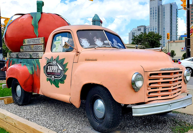 Vintage peach Studebaker truck with anthropomorphic cartoon smiling giant tomato