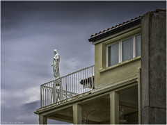 A statue of Jesus on a balcony looking out over the neighborhood