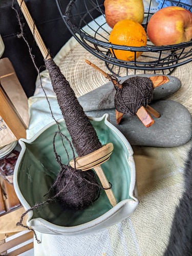 A yarn bowl with 2-strand plying ball also holds turned Andean pushka with cop of plied yarn by irieknit.  A Jenkins Lark spindle with a cop of the same Zwartables yarn rests on rocks from Lake Ontario on a kitchen table.