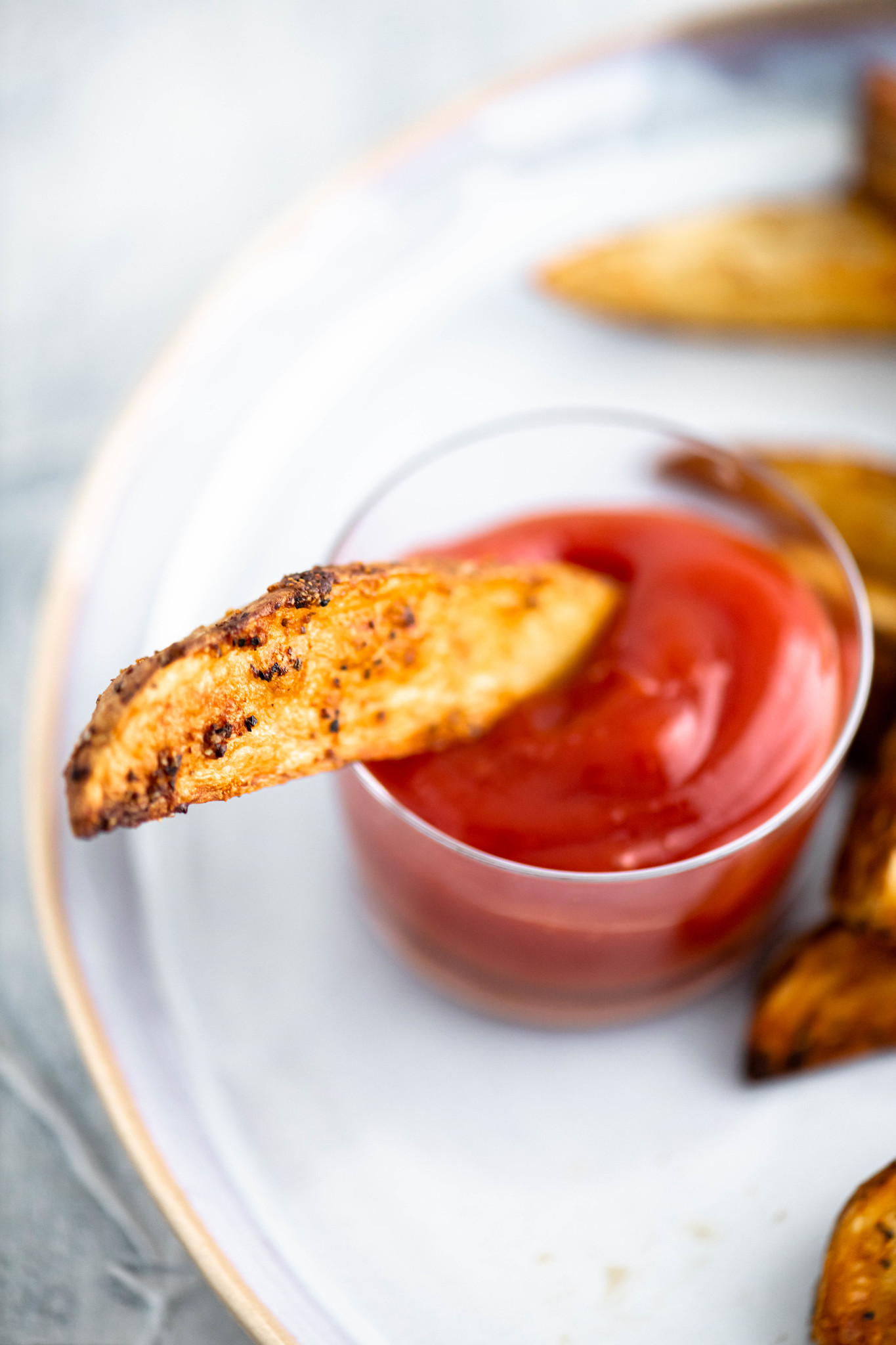 Air fryer potato wedge dipped in a small glass bowl of ketchup.