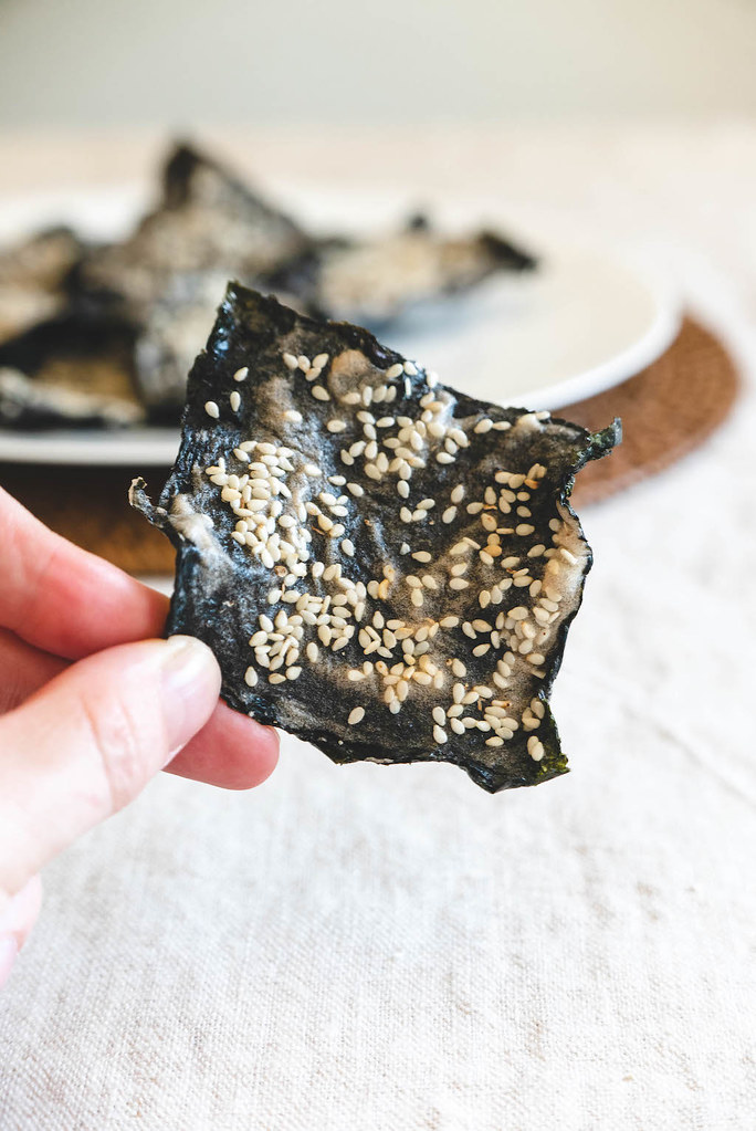 Holding up dried seaweed coated with sesame seeds by hand.