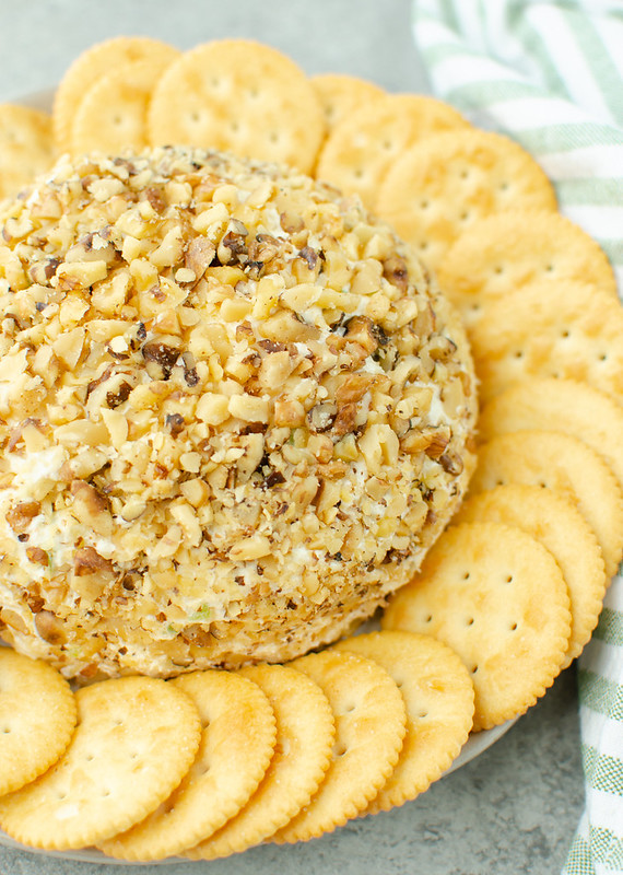 Top view of cheese ball coated in walnuts on a white plate; Ritz crackers around it