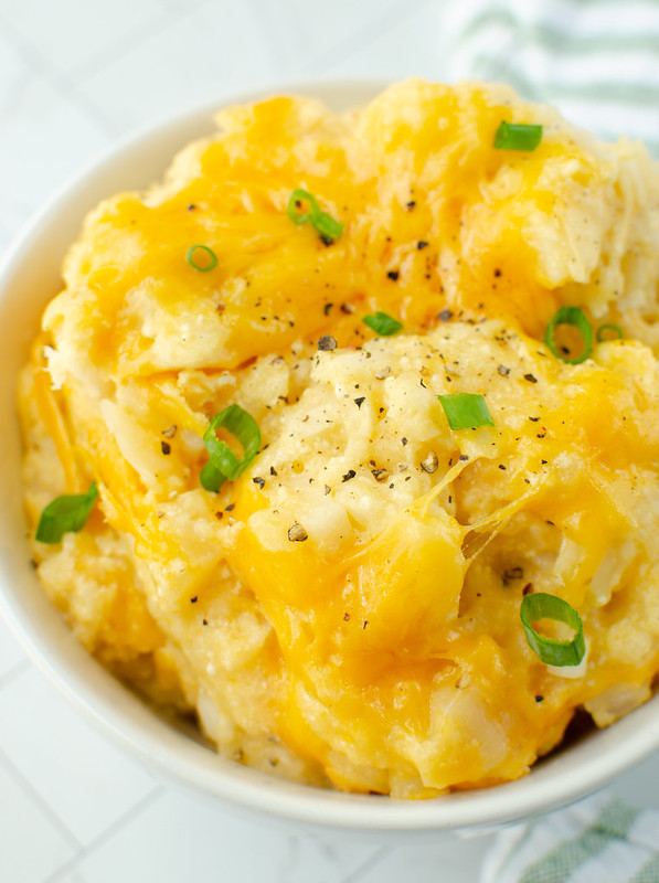 Diced potatoes with cheese, cream of chicken soup, green onions, and black pepper in a white bowl