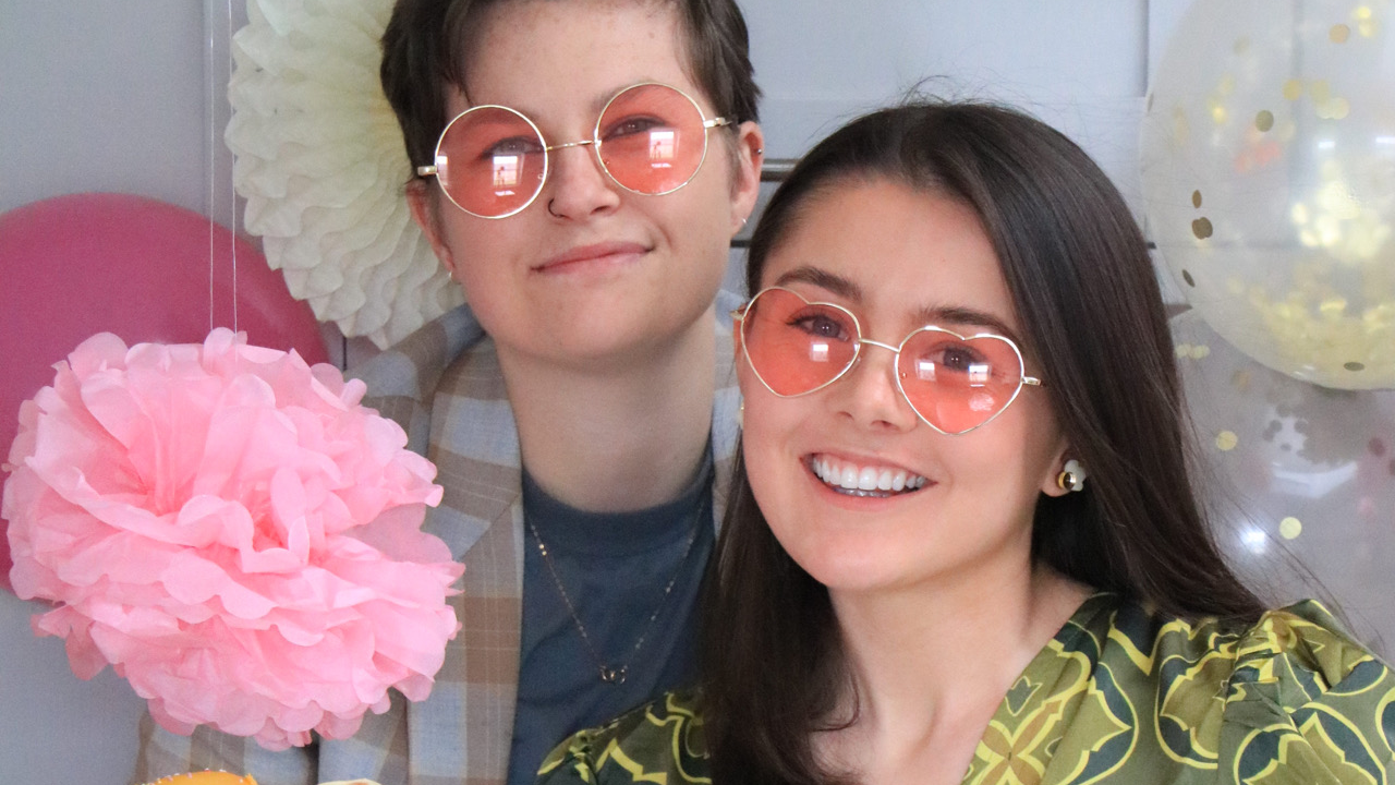 Two people posing in pink sunglasses surrounded by balloons