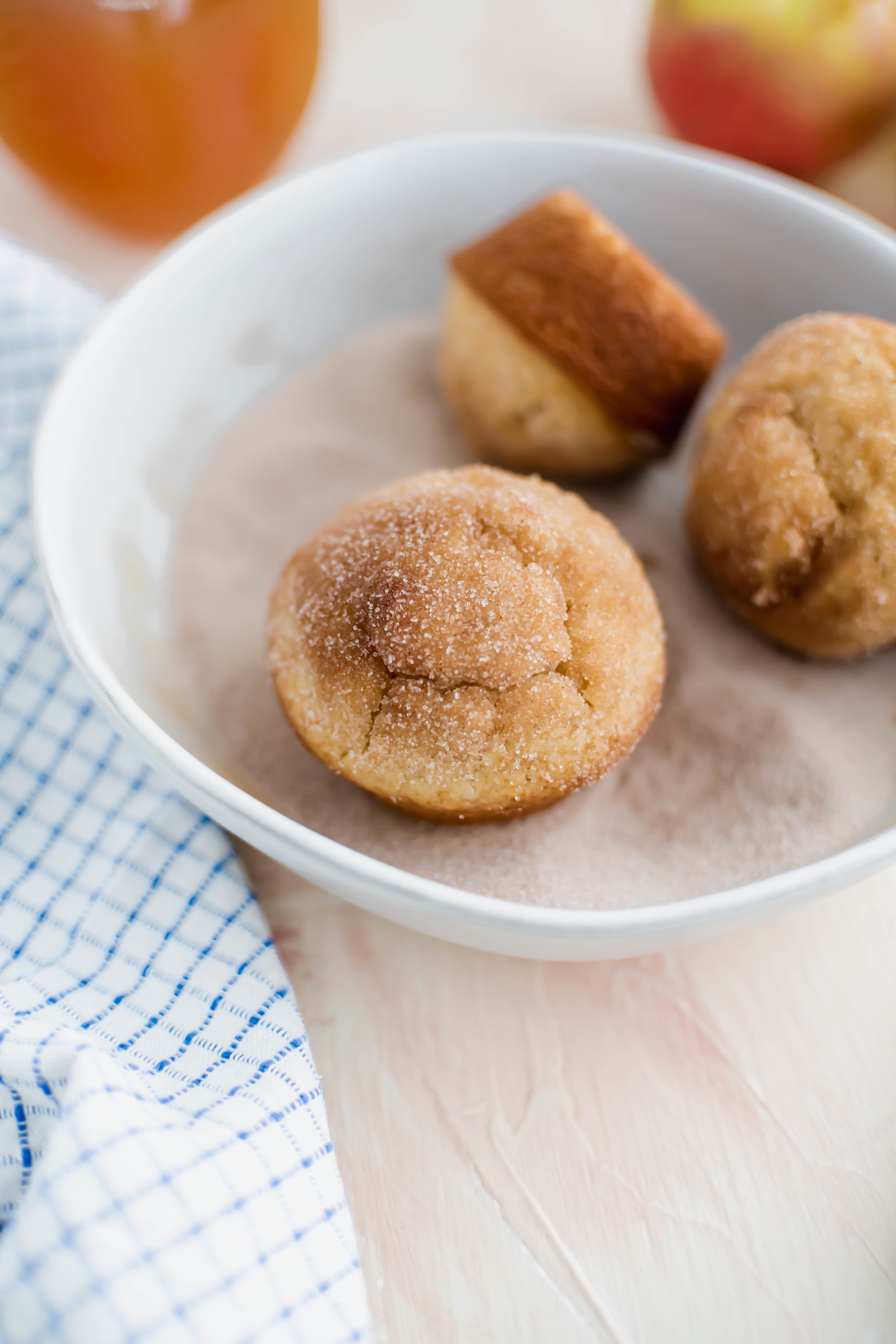 Three apple cider muffins in a bowl of cinnamon sugar to show texture of tops.