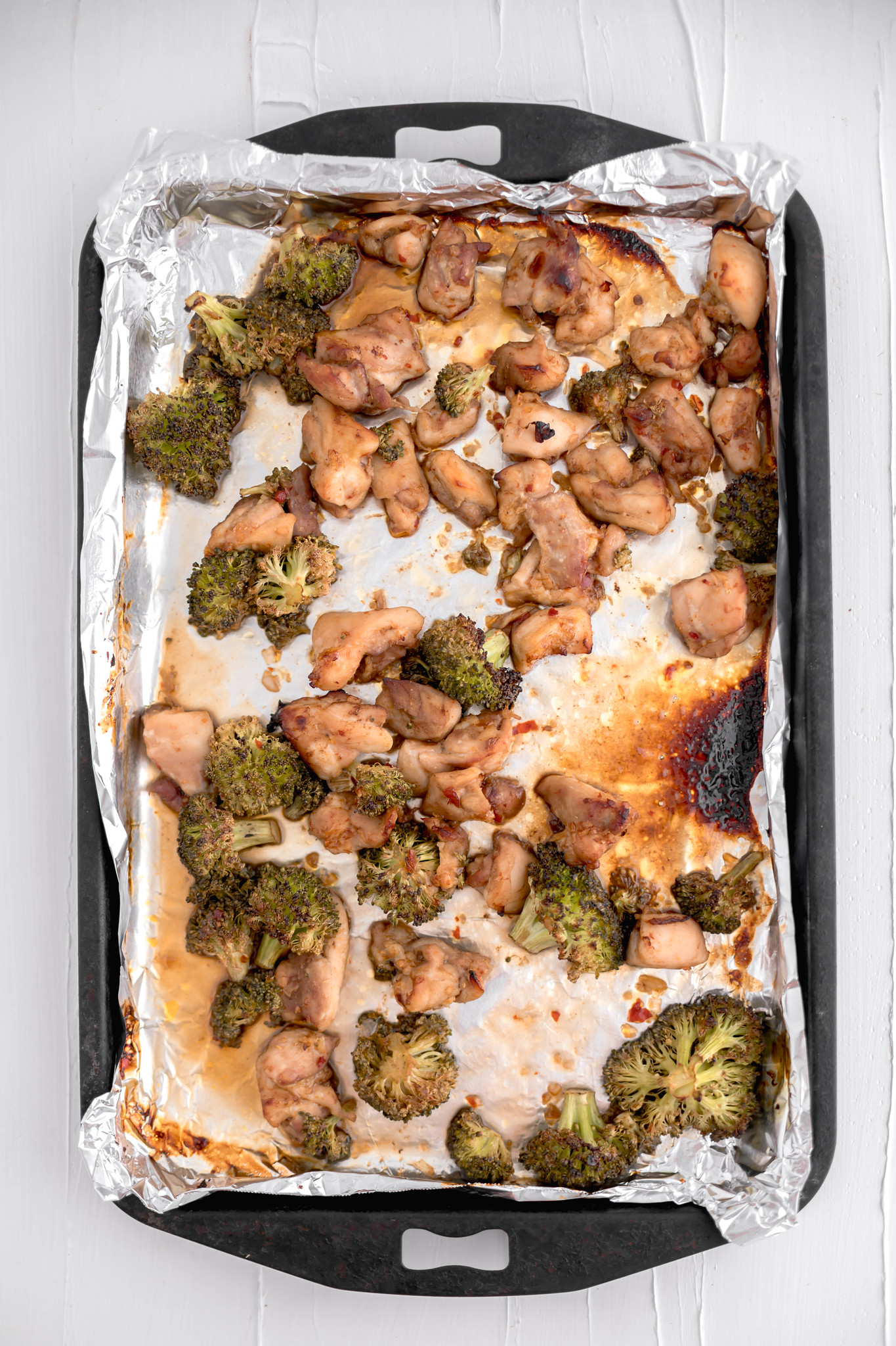 Chicken and broccoli baked in a sweet chili sauce on a foil lined baking sheet.