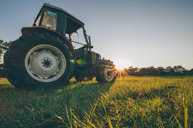 Tractor on a grass field with beams of light next to it coming from the setting sun