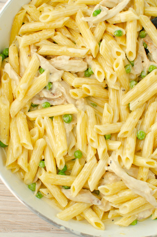Overhead shot of pasta, chicken, and peas in alfredo sauce in a white skillet