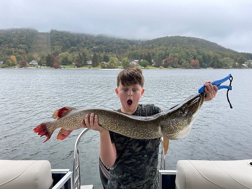 Boy on a lakeside dock holding a large northern pike