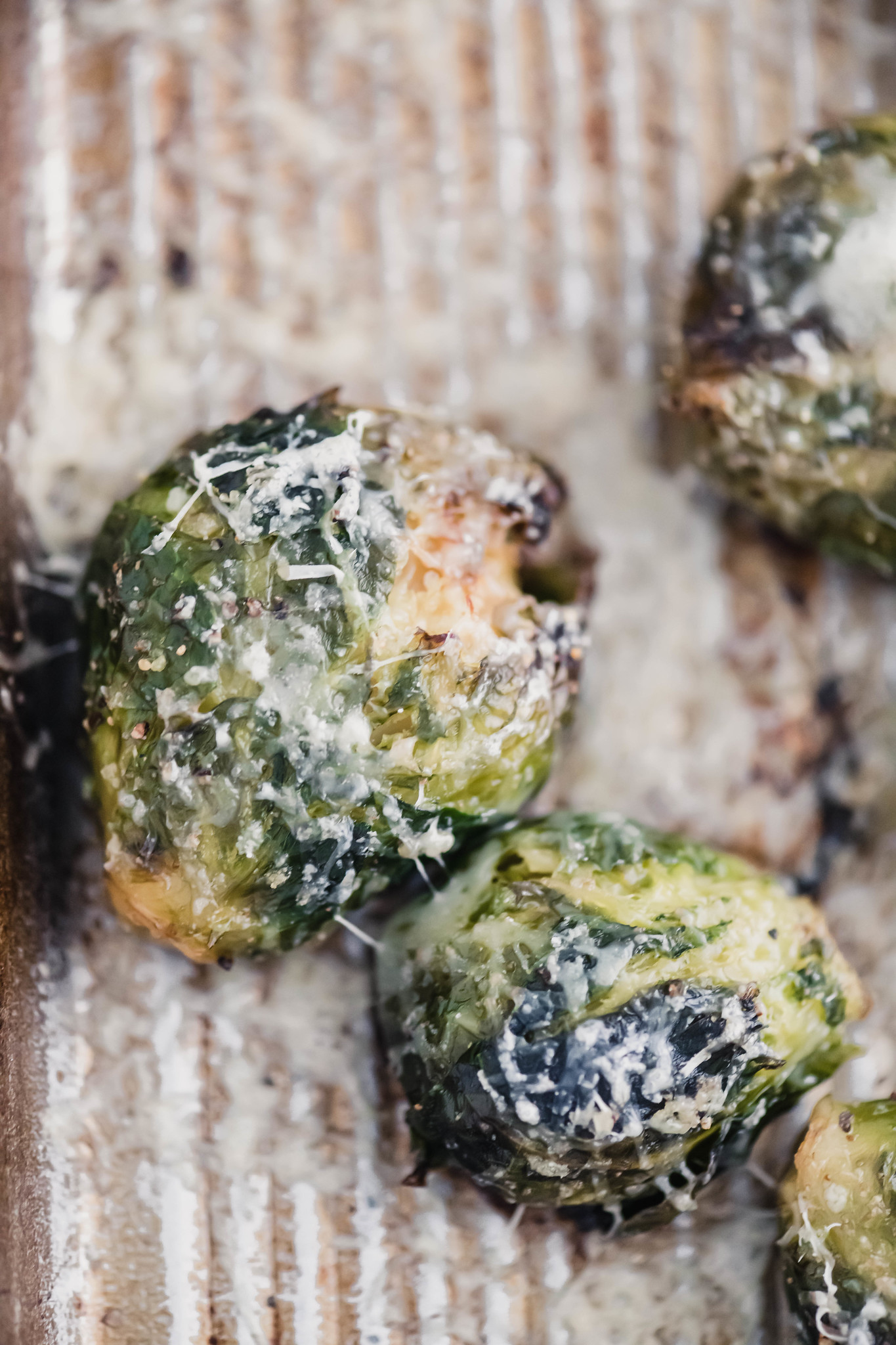Close up of two parmesan smashed brussels sprouts on baking sheet.