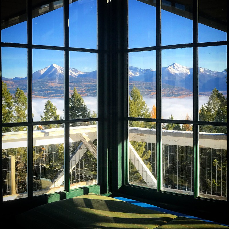 Looking out the windows of a firelookout at snow dusted peaks beyond.