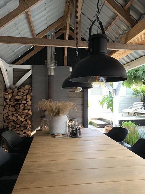 Hanglampen boven tafel in overkapping kruik met takken houtopslag onderzetters