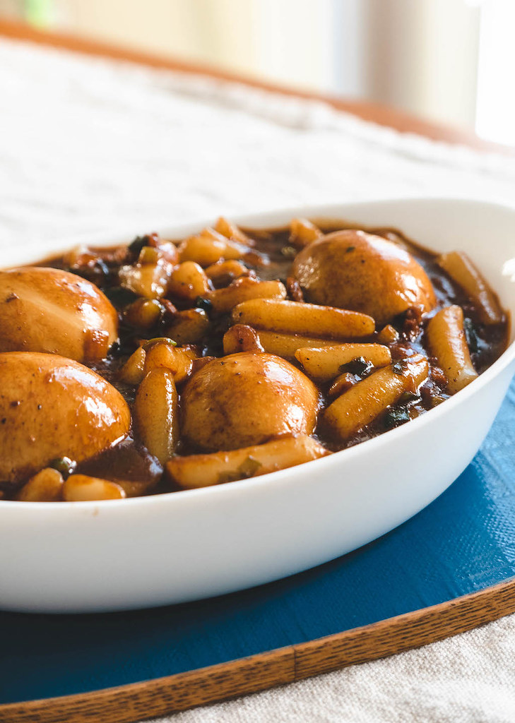 A close up side shot of the Korean rice cakes in black bean sauce in a white bowl on a blue tray. 