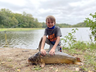 Photo a boy next to a large carp, on the shore of a lake