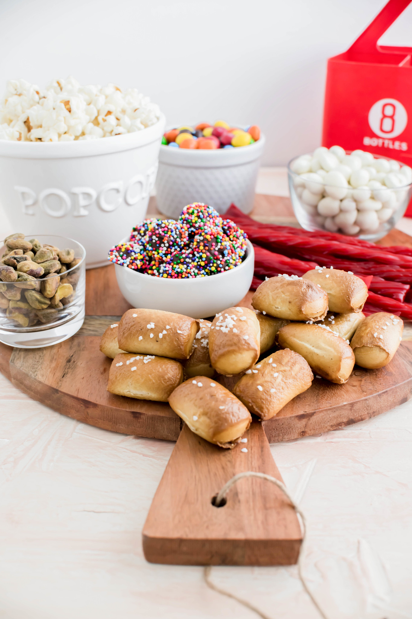 Movie night snack board filled with bowls of popcorn, yogurt raisins, M&M's, pistachios and snowcaps. Soft pretzels and twizzlers on the board.