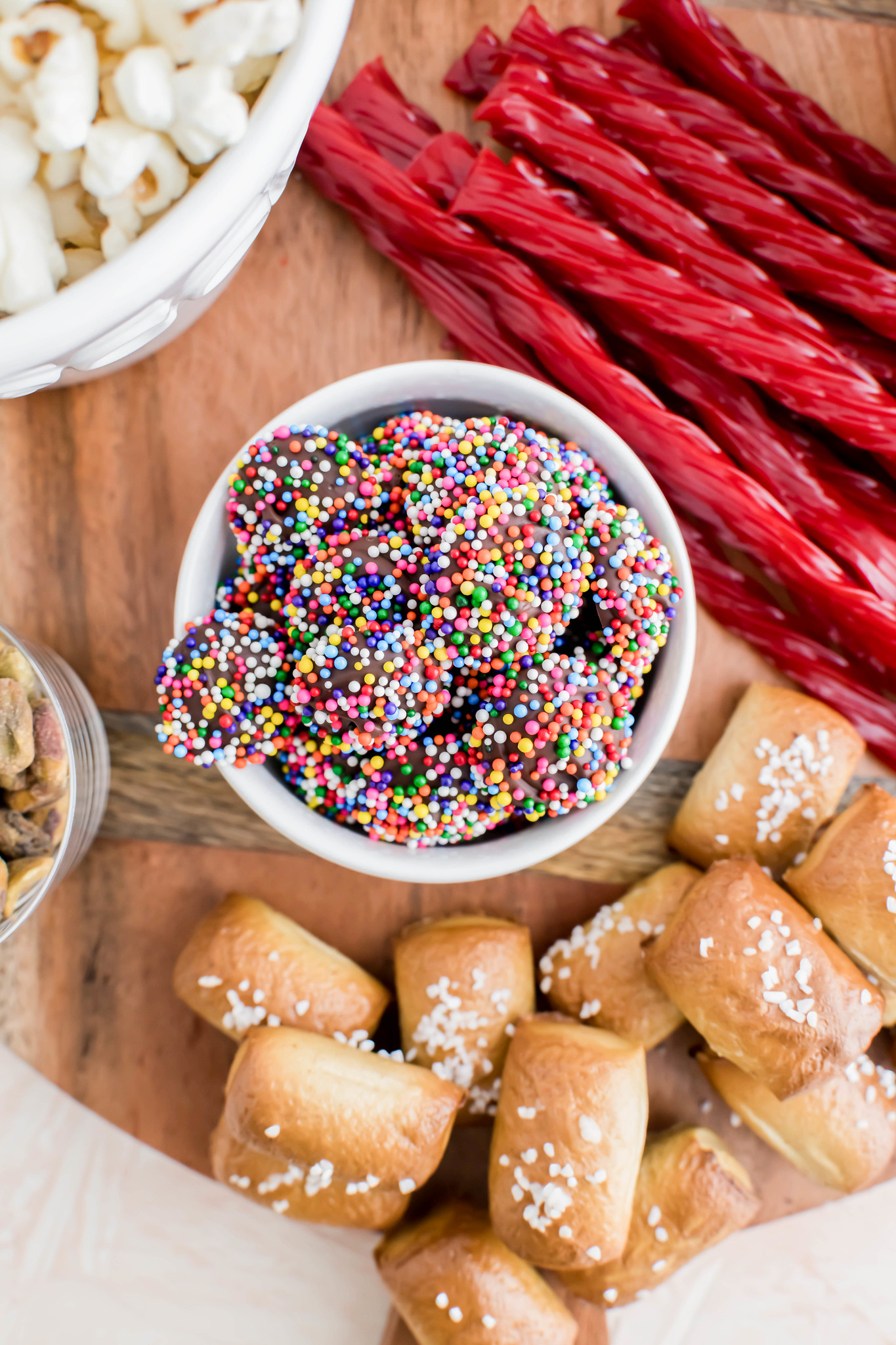 Bowl of colorful snowcaps on a wooden board surrounded by twizzlers, soft pretzels.
