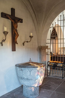 Vorhalle im Erdgeschoss des Turms: Taufstein aus Basaltlava (12. Jh.) und Kruzifix (18. Jh.) zwischen barocken Leuchtern