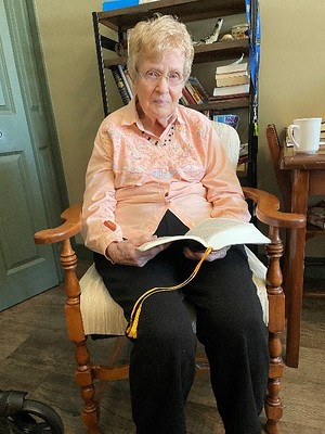 Betty sits with a book in her lap while wearing a peach button up.