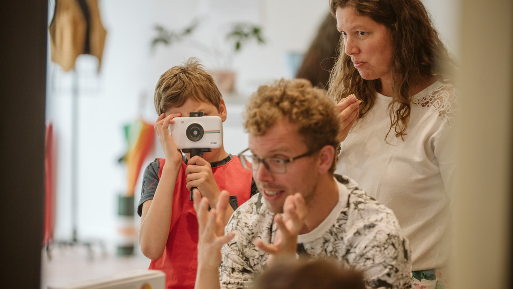 A male scientist talking with a young person at a table who is taking part in an activity using a polaroid camera