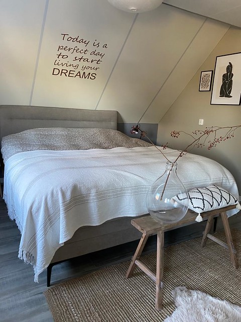 Slaapkamer schuine wand tekst muur landelijke slaapkamer fles met rozenbottel tak houten bankje achter bed