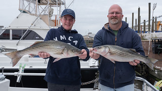 Two men each hold up a large striped bass they caught
