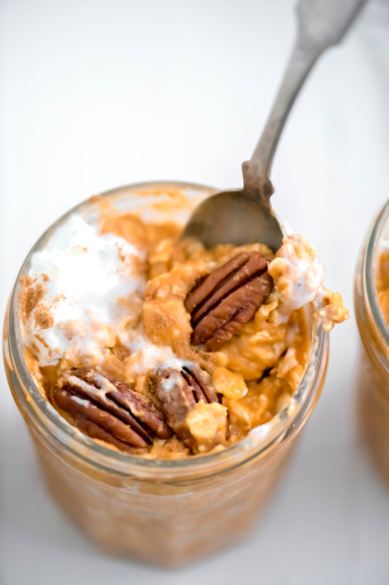 Close up of spoon in jar of pumpkin overnight oats with pecans and whipped cream.