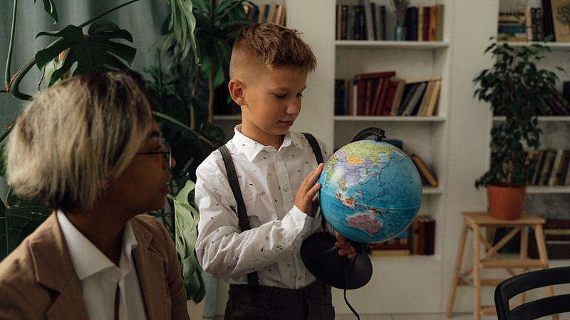 A child holding a globe pointing and staring it in while an older relative overlooks