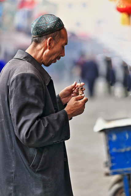 Thin-bearded Uyghur man eating a mutton skewer at Hotan's Sunday market. Xinjiang-China-0091