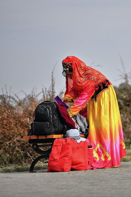 Yugur woman in ethnic attire with terai hat absorbed in luggage reordering. Mati Si complex-Zhangye-Gansu-China-1012