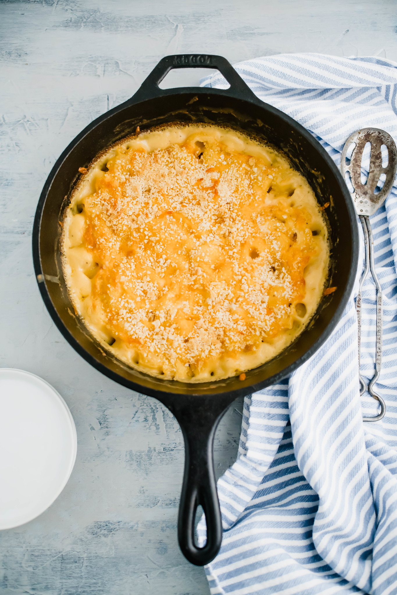 Cast iron skillet baked macaroni and cheese. Cloth napkin and large serving spoon to the right side. 