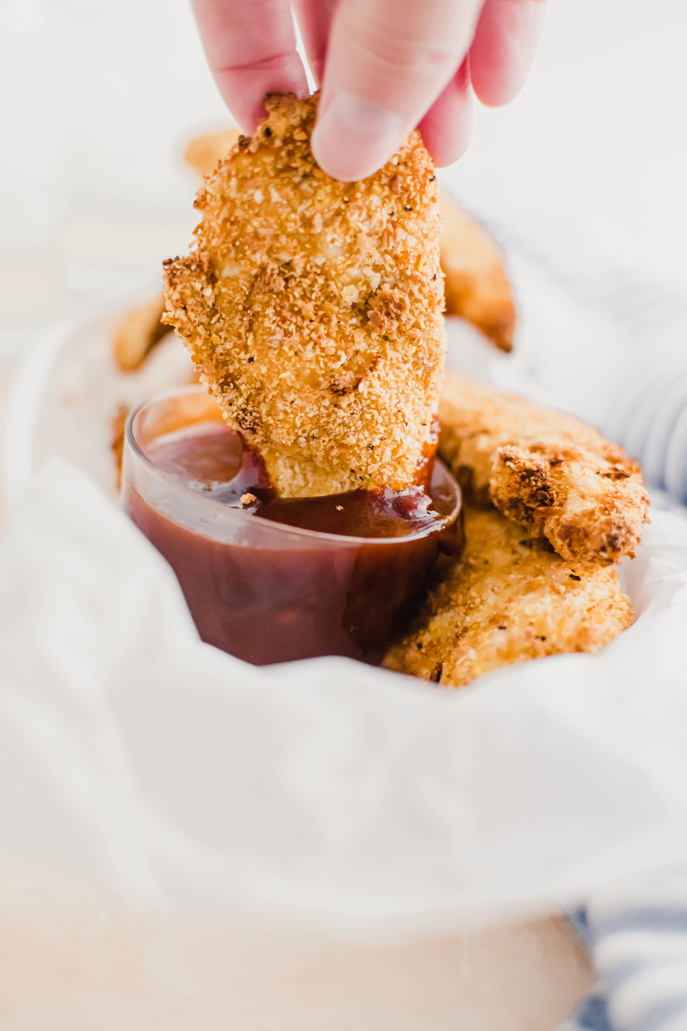 Hand dipping chicken tender into a glass bowl of barbecue sauce.