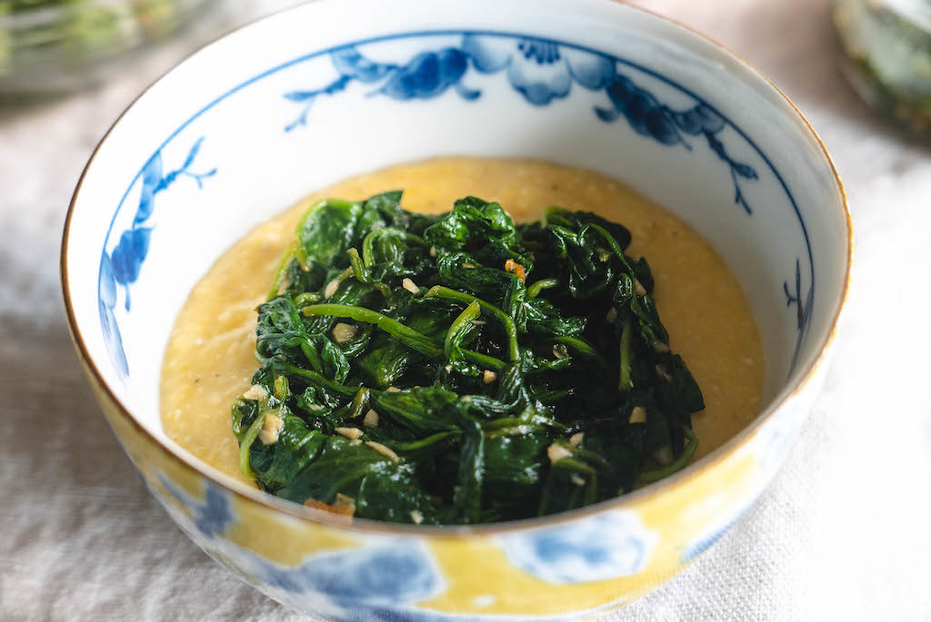 A photo of a bowl of yellow grits topped with sautéed spinach.