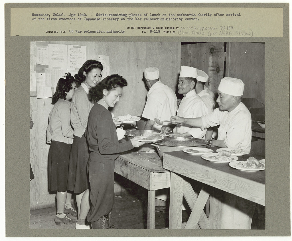 Manzanar, Calif. Apr. 1942. Girls receiving plates of lunch at the cafeteria shortly after arrival of the first evacuees of Japanese ancestry at the the War Relocation Authority center (LOC)