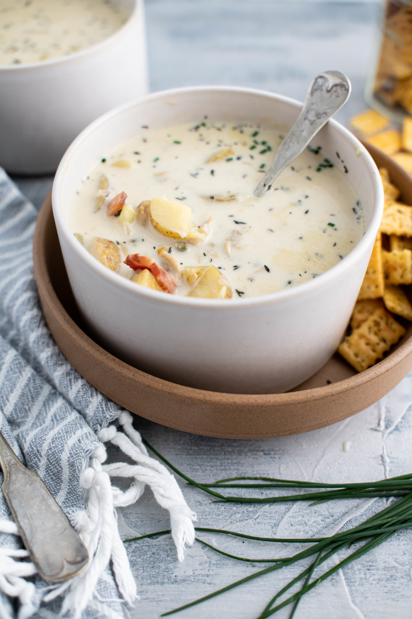 Large white bowl filled with instant pot clam chowder and set on a larger clay colored plate with crackers on the side.