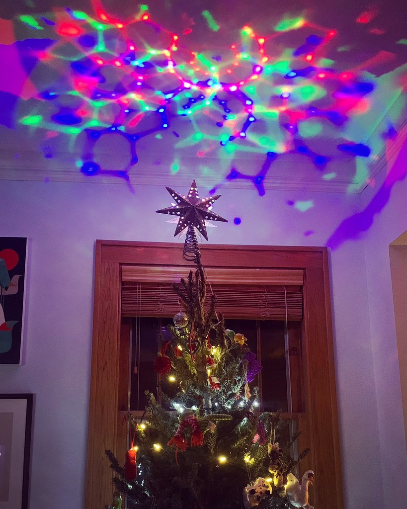 A Christmas tree decorated with a tree topper that produces colorful psychedelic light patterns on the ceiling