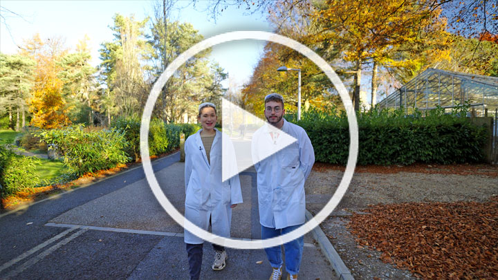 Two students in lab coats walking on campus