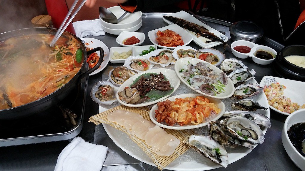 A shot of a Korean seafood meal-- a table filled with oysters, octopus, stew, scallops, and more!