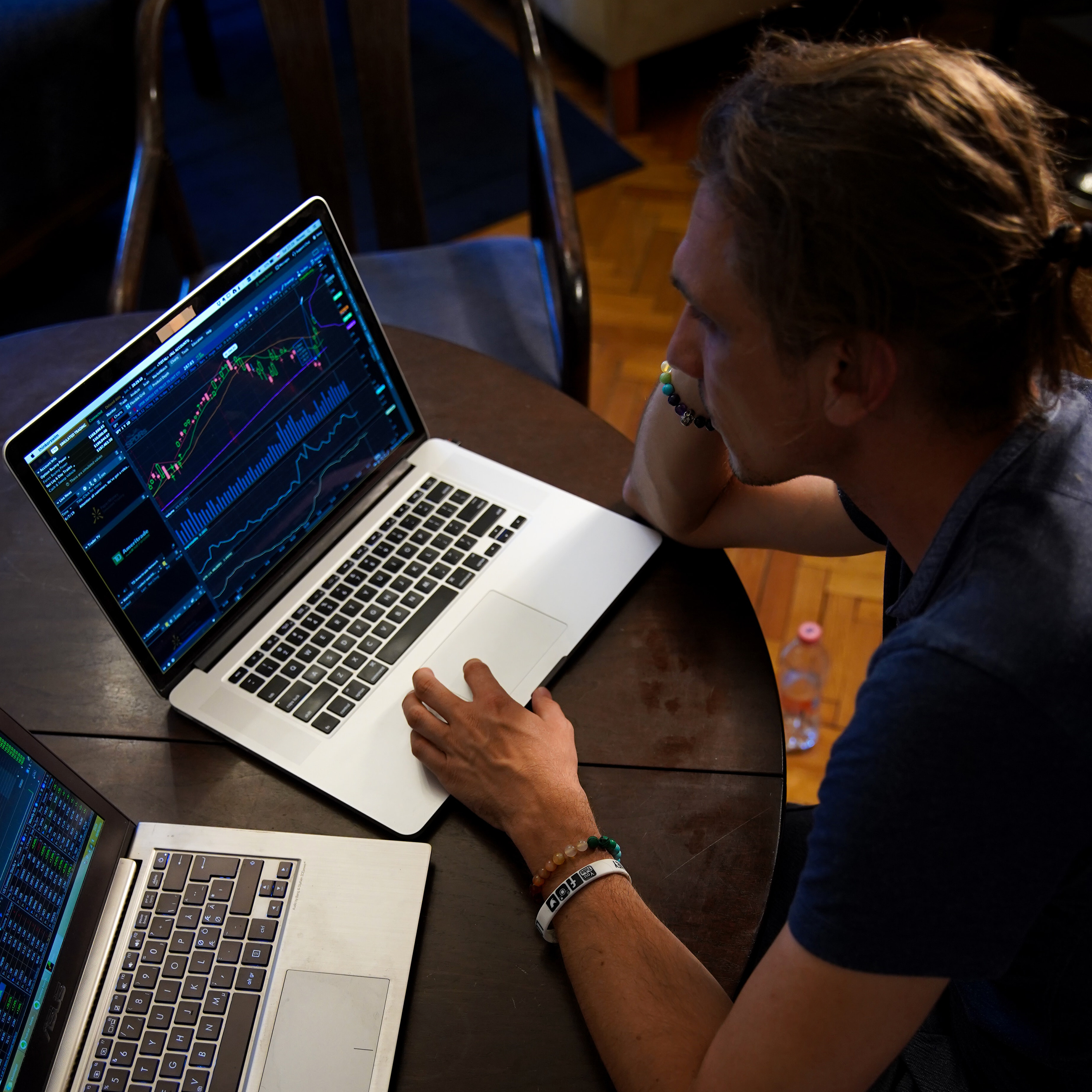 Man sitting at a table looking at financial charts on two laptops