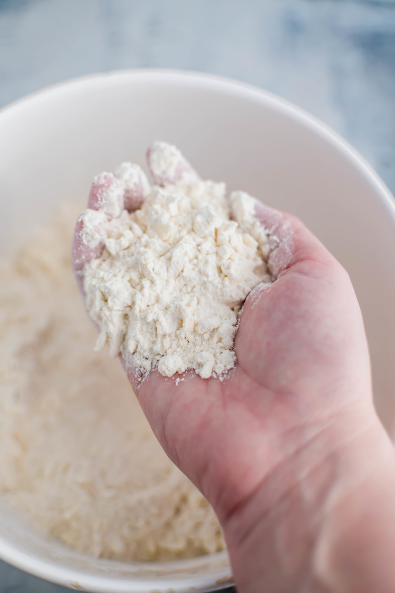 Flour and butter mixed together. Hand lifting it out of the bowl to show the texture.
