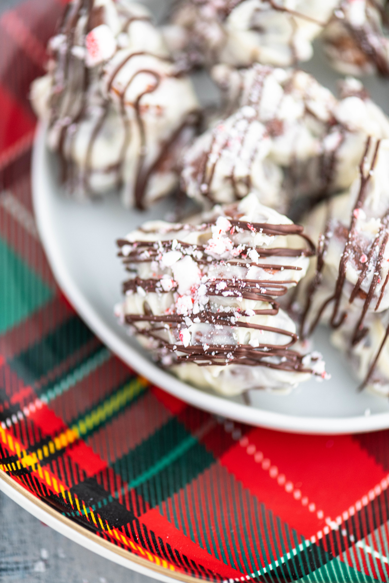 Close up of peppermint bark almond cluster on a small white plate with a plaid Christmas charger.