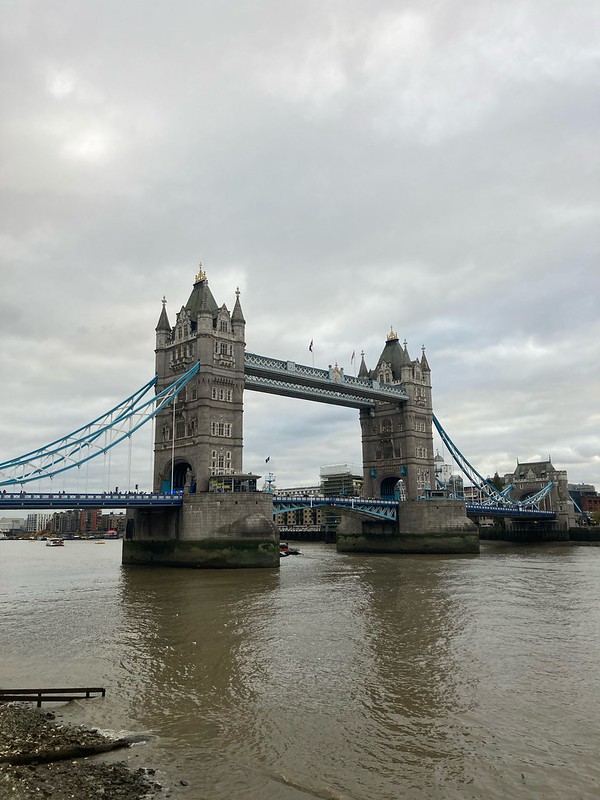The decadent Tower Bridge, over a river of green gray water on a cloudy day in London.
