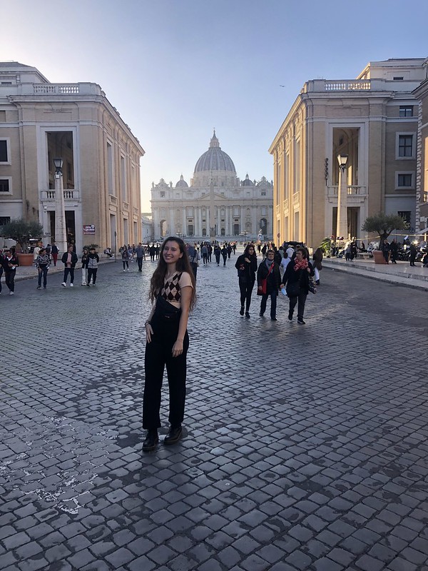 Shea posing on a stone street in Rome in a plaza in front of a domed building.