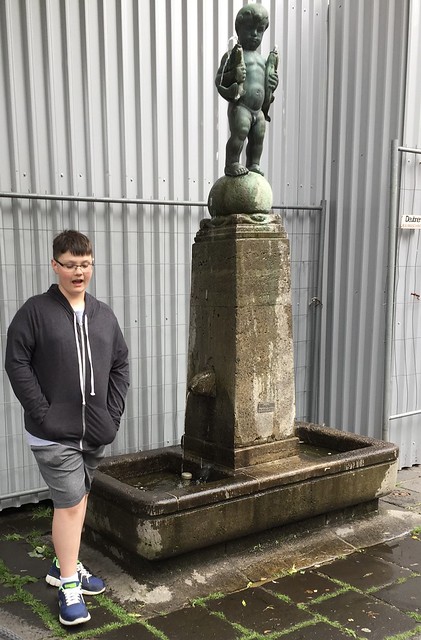My grandson Miles standing beside the statue in Aachen located to the side of a street near the Aachener D.o.m. , Martin’s photograph , Aachen , Germany , June 9. 2019